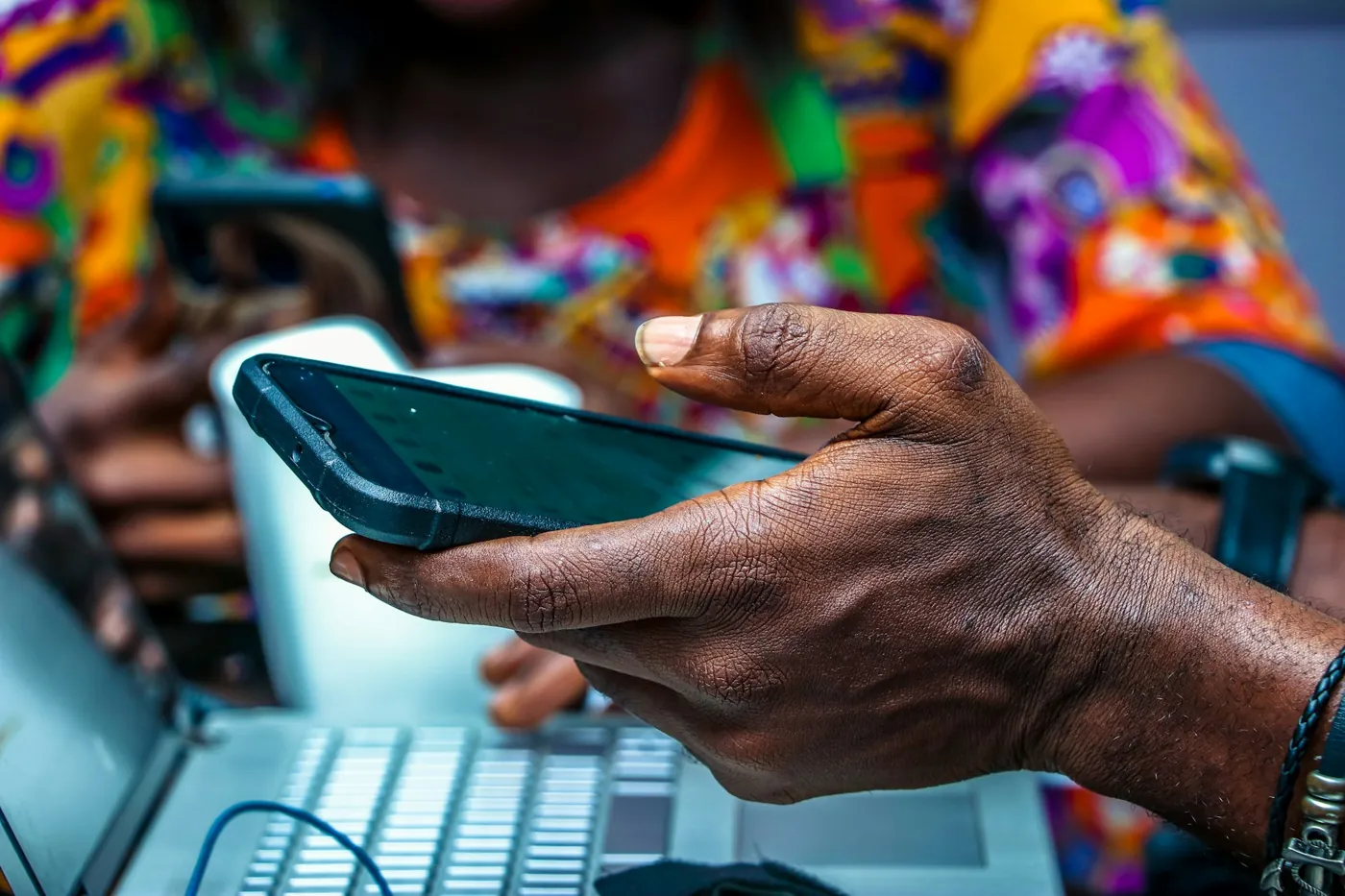 Hands holding a smartphone beside a laptop